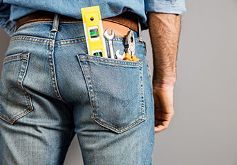 Male is standing in denim clothes with hand tools for repairment in jeans. Isolated on grey background